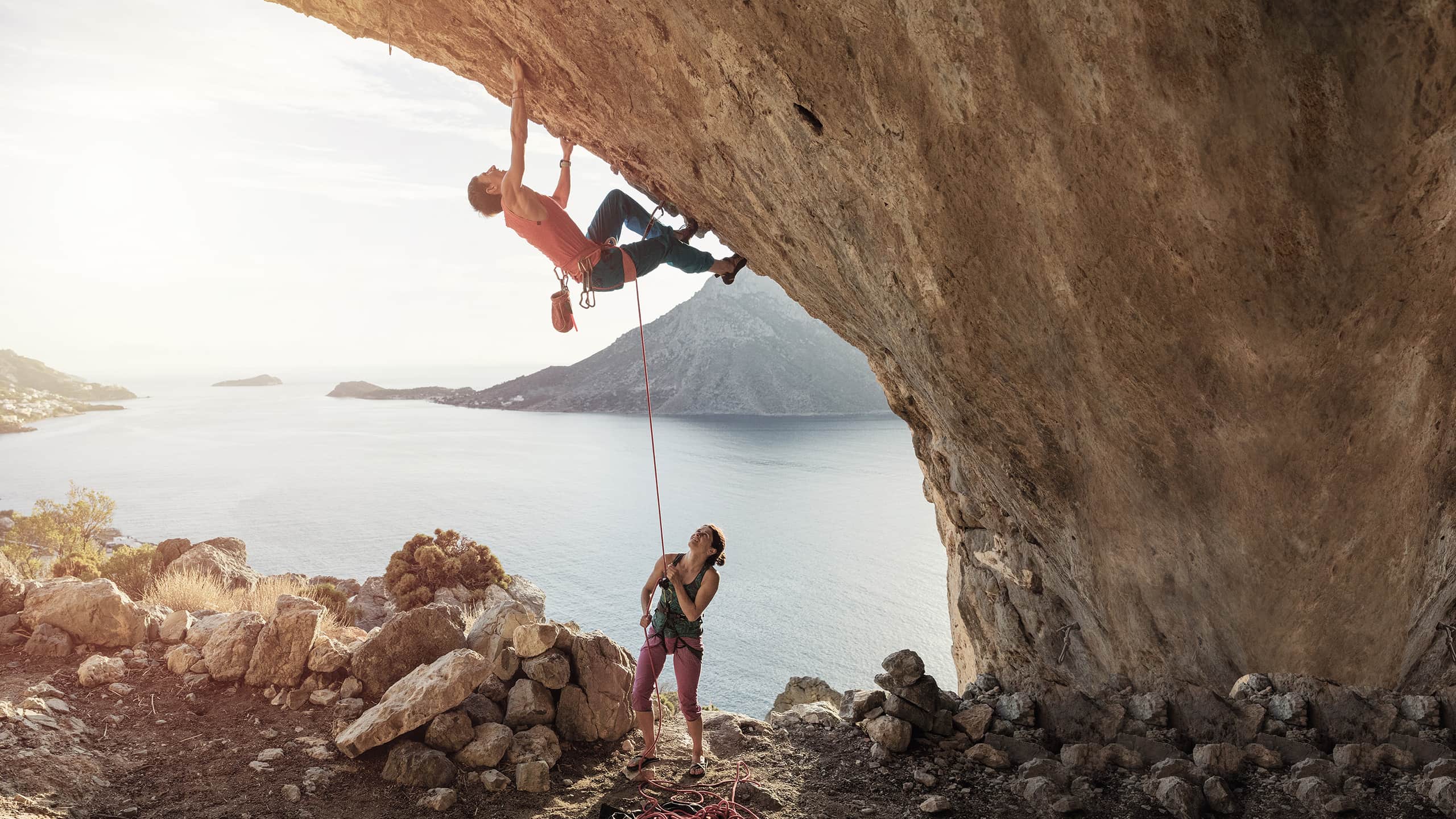 Mann klettert eine Steilwand hoch und wird von einer Frau mit einem Seil gesichert